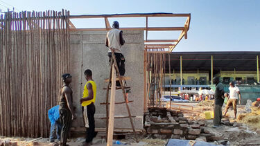 One builder standing on a ladder next to the sustainable cold room while two other people stand nearby