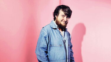 Tim Key wearing a light blue denim jacket against a pink wall