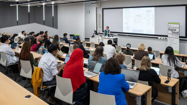 Dorothea Kleine giving a presentation at the front of a busy lecture theatre