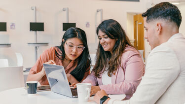 Two female students and a male sat around a laptop 