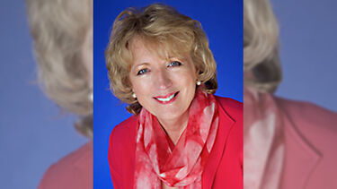 A headshot of Amanda Stevens smiling against a blue background while wearing a red jacket and scarf