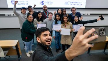Ahmed smiling and standing in front of a group of Hackathon students to take a group selfie