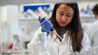 Student in a white lab coat using a pipette