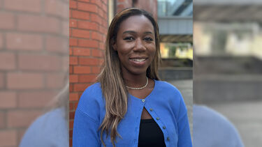A headshot of Tia smiling outdoors on campus, wearing a blue cardigan