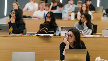 A student sat in a lecture hall looking listening to a speaker and making notes on a laptop