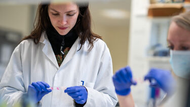 Image of student in a white lab coat holding a test tube 