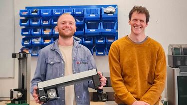 Two males holding rail engineering device in workshop 
