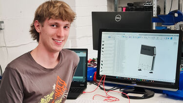 Man in front of computer smiling in workshop for photo