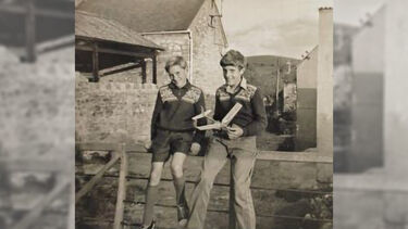 Black-and-white shot of brothers David and John as youngsters, sitting on a farm gate