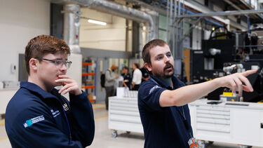 Two men in dark blue jackets looking and pointing at a machine