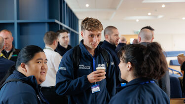 Three people in dark blue jackets stand talking and holding coffee