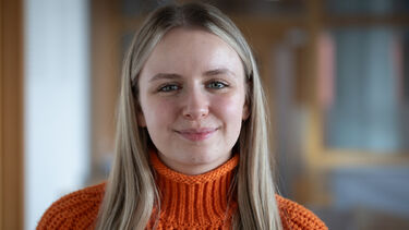 headshot of Teri smiling in a library - she is wearing long blonde hair and an orange knitted jumper