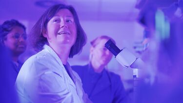 Heather Mortiboys in a lab coat looks up from microscope