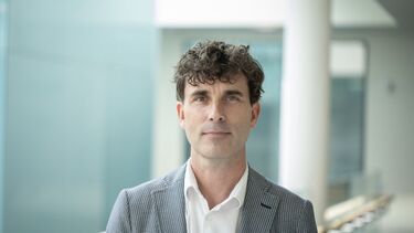 A person smiling at the camera in a grey suit.