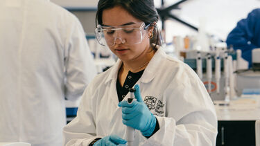 Person wearing lab PPE using a pipette to dispense liquids