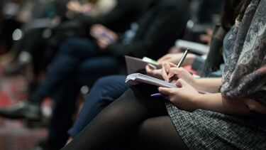 Rows of chair with people sat in them and writing notes in a notepad 