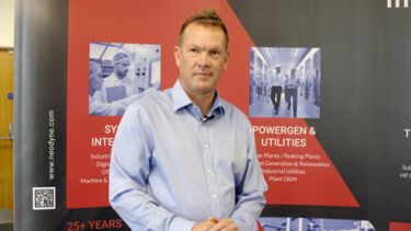 Matt stands in front of a backdrop with information on the company behind him. He wears a light blue shirt.