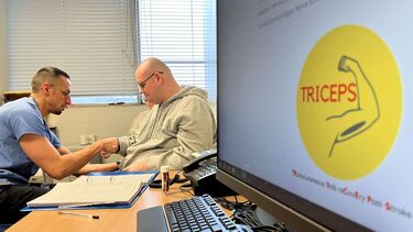Logo of the Triceps trial on a computer screen with a doctor and patient sitting in the background.