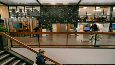 Western Bank Library reception - student walks down the staircase and colleague is standing at reception
