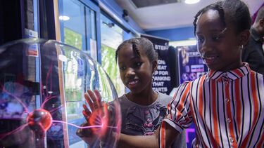 Two young children are interacting with a static ball, which is creating red beams of light.