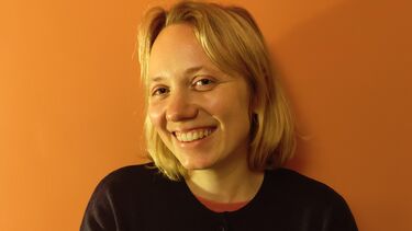 Mari- Liis standing in front of an orange wall smiling