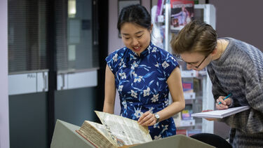 Two students standing over archival document and reading 