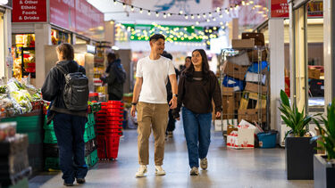 Two smiling people walk side by side through a bustling indoor market in Sheffield