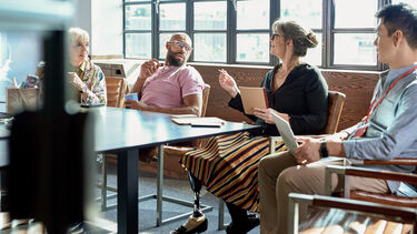 A group of people sat around a meeting room desk, one of the people has a prosthetic leg