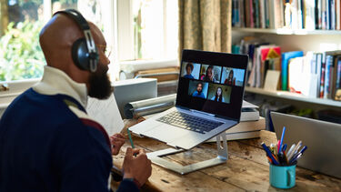 A person sat at a desk in front of a laptop, with a video call on the screen.