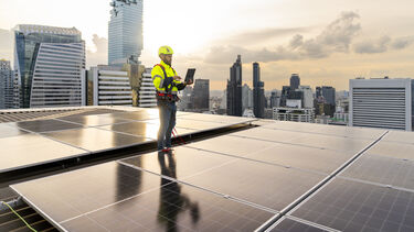 Man in hard hat on rooftop of solar powered building, holding laptop