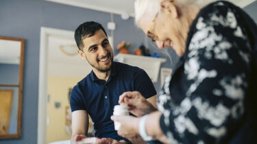  Smiling man sat with elderly woman holding tablets in a jar.