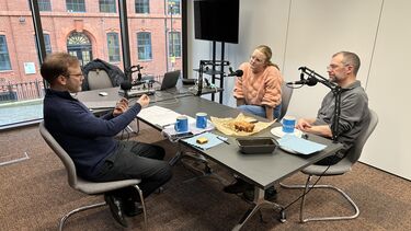 Three people sat around a table recording a podcast with professional microphones