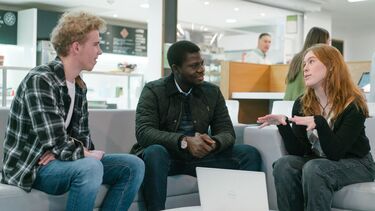 Three students sitting on a sofas with a laptop open between them
