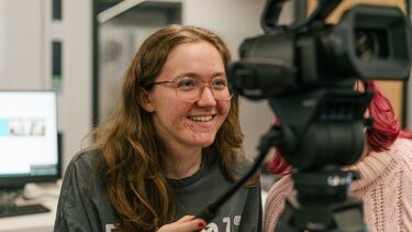 Girl in glasses behind video camera