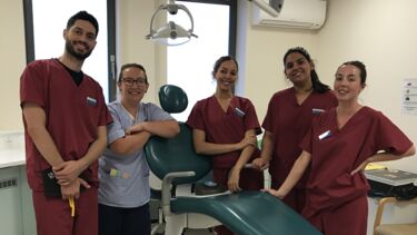 A group of four students in scrubs next to a dental clinician leaning on a dental chair.