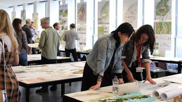 A student and teacher inspecting an architectural drawing at a busy exhibition
