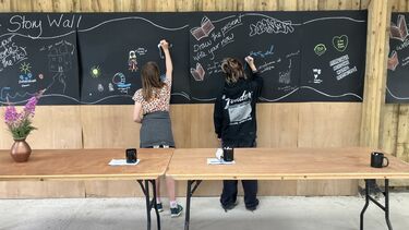 Two people annotating a story wall on a long blackboard