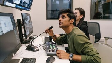 Student speaking into a microphone looking at computer screens