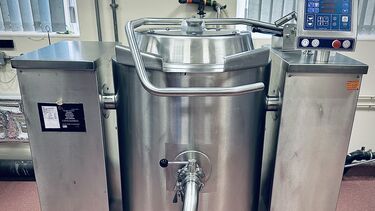 A stainless steel industrial steam generating cooking kettle.