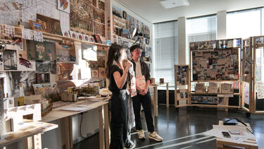 Two students showcasing their architectural drawings and models in studio