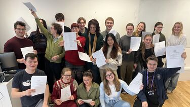 Group of about 20 students with white paper in their hands, quite informally arranged