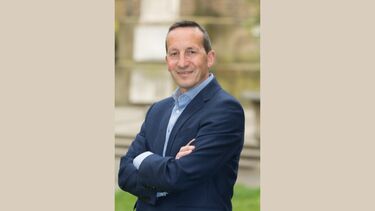 Tim Jotischky stands with his arms folded, against a beige background