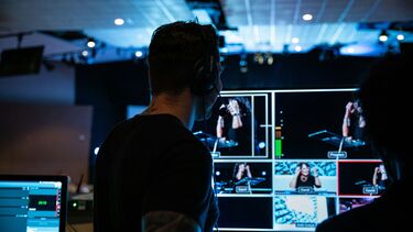 A TV producer with a headset watches multiple angles of a woman talking behind a lectern