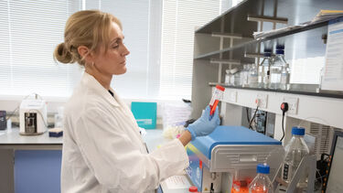 A woman in a research lab, wearing a lab coat, holding a tube of liquid.
