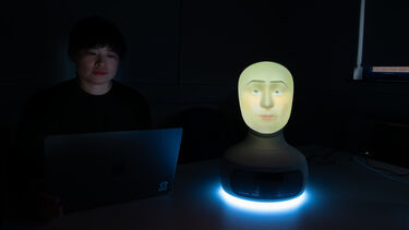 A researcher sitting at a computer programming a robot face