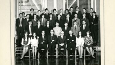 A group of people sitting and standing on rows of chairs