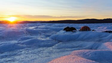 Three tents on a glacier at sunrise