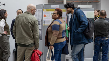 Three people talking in front of a research poster