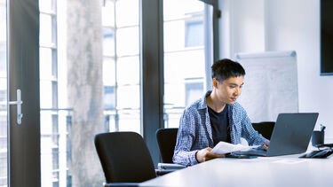 A student sits in a room and looks at a laptop on the table.