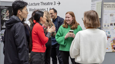 Four people talking near a research poster